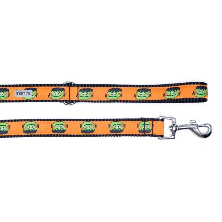 A dog leash with a black background with an orange ribbon with a Frankenstein head