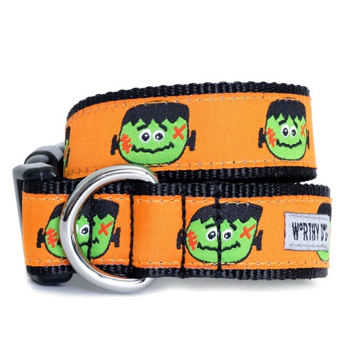 A dog collar with a black background with an orange ribbon with a Frankenstein head