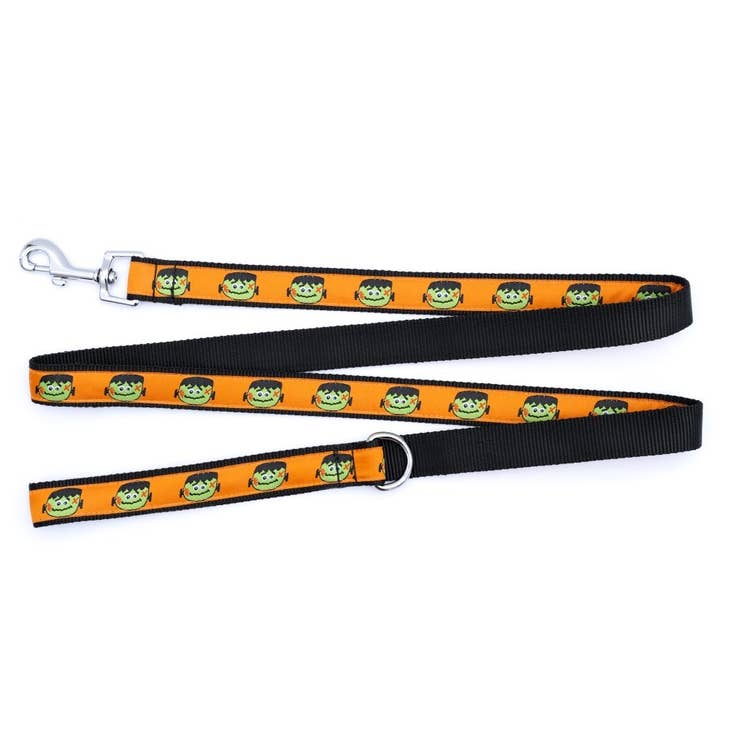 A dog leash with a black background with an orange ribbon with a Frankenstein head