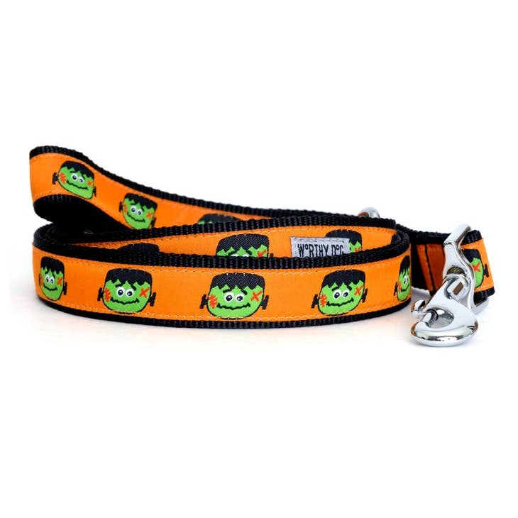 A dog leash with a black background with an orange ribbon with a Frankenstein head